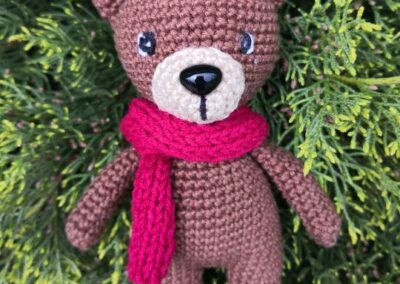 Horgolt amigurumi maci piros sállal, zöld háttér előtt